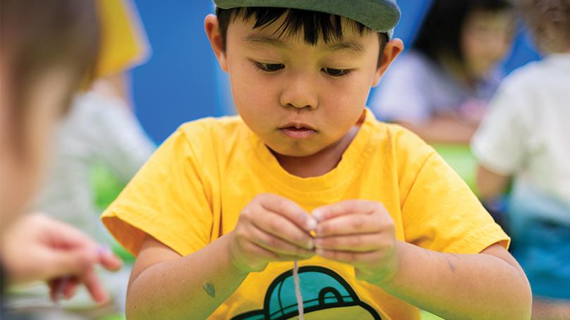 Young boy with yellow shirt puts beads on string