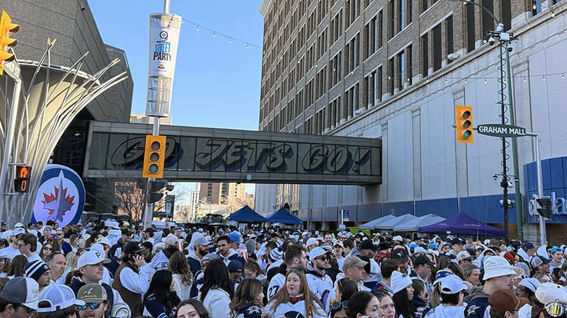 People standing on a street wearing Winnipeg Jets clothing standing in front of a skywalk painted with 'Go Jets Go' design