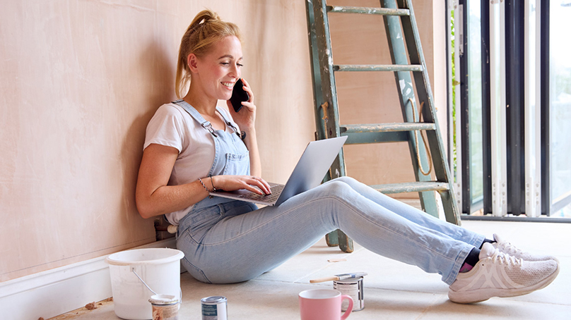 Woman sitting in a room under construction with a phone and laptop