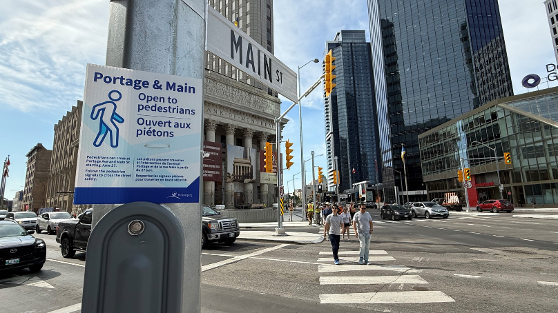 Two pedestrians crossing the street at the intersection of Portage and Main