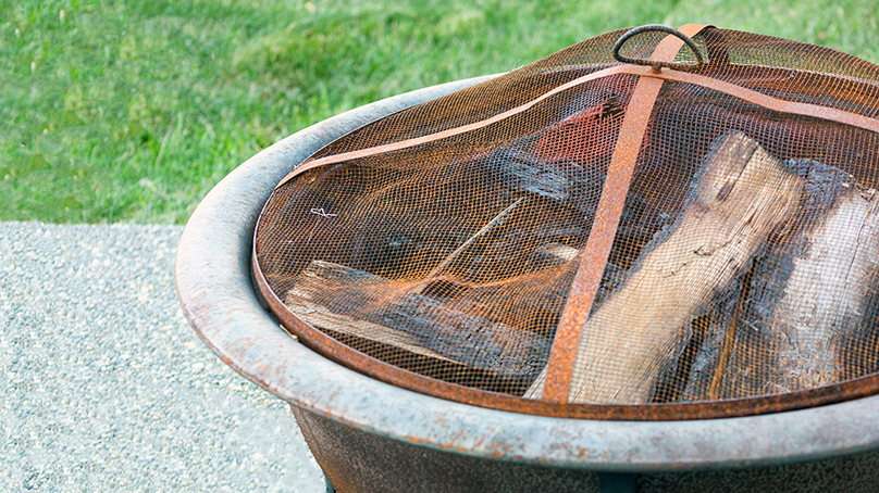 Fire pit with a mesh grate on top sitting on a paving stone
