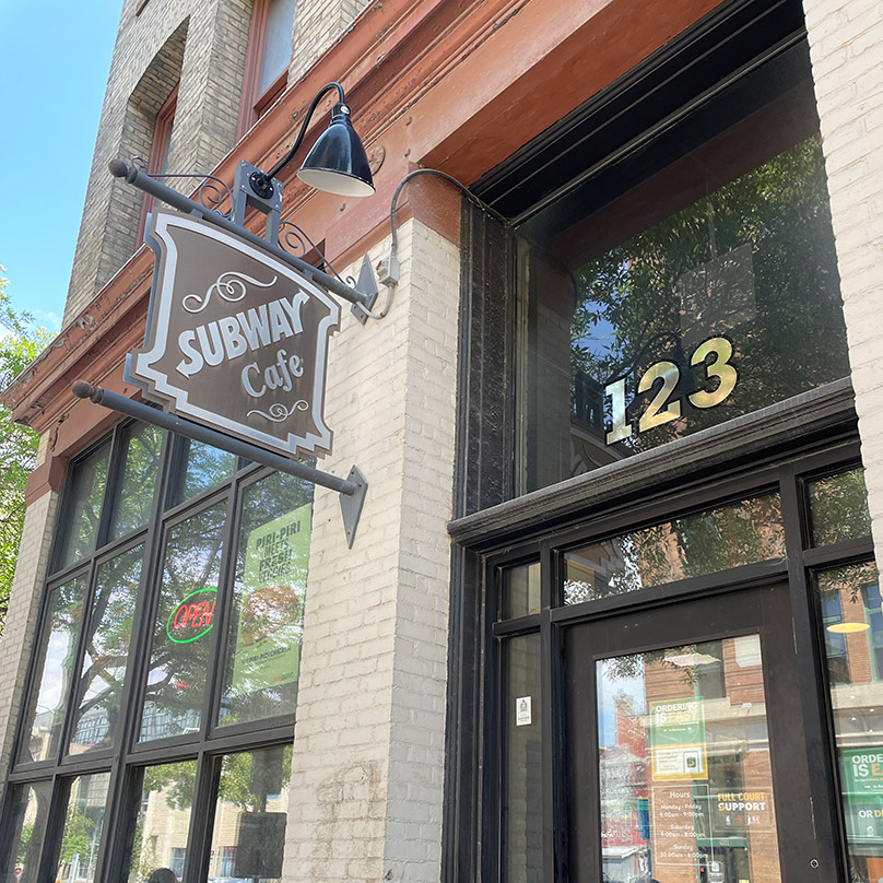 The Subway Café sign uses external gooseneck lamps to resemble a traditional light source.