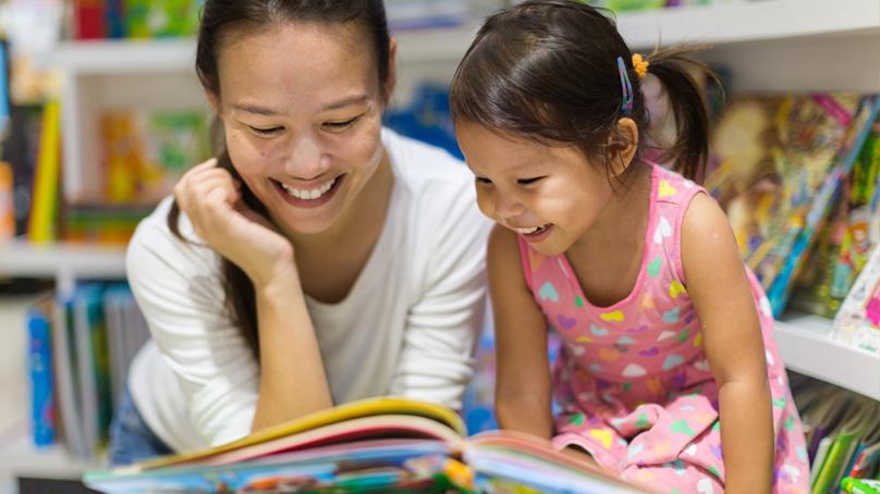 Woman and young girl reading books in a library