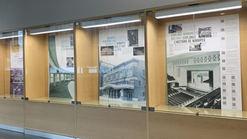 Panels of the Winnipeg 150 History Exhibit are seen behind glass.