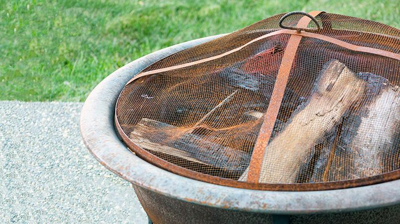 Fire pit with a mesh grate on top sitting on a paving stone