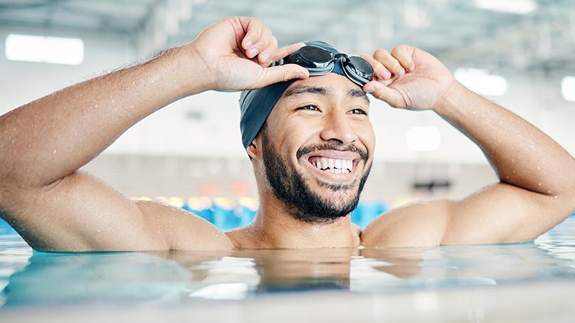 Smiling man in pool adjusting swim goggles on head