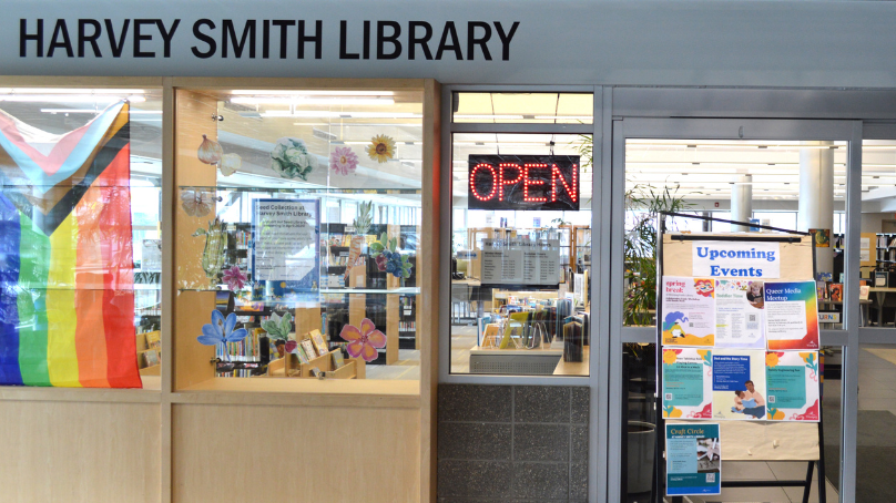 Entrance to Harvey Smith Library in the Cindy Klassen Recreation Centre. A pride flag hangs in the display window and the open sign on.