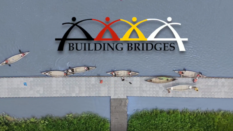 Canoes along the shoreline with Building Bridges logo overlaid